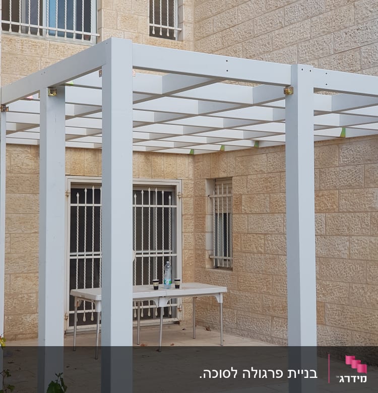 פרגולה לבנה עם שולחן פלסטיק וכוסות על המרפסת